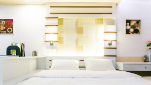 A modern bedroom with a large bed, a bedside table, a nightstand, and a wall-mounted shelf with books and a decorative item. - Sunset Residence Pinklao (Bangkok)