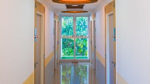 A hallway with a modern ceiling design, doors on both sides, and a view of greenery outside. - Sunset Residence Pinklao (Bangkok)