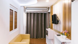 A modern hotel room with a yellow sofa, a white console table with a TV, a small plant, and a mirror with a decorative frame. - Sunset Residence Pinklao (Bangkok)
