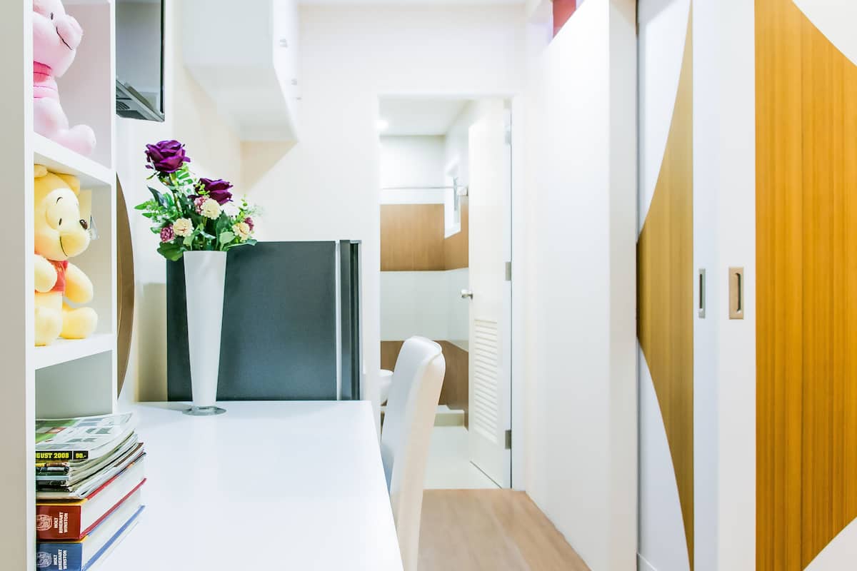 A modern, well-lit hallway with a white desk, a vase of flowers, and a plush toy on the left.