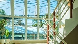 A staircase with wooden steps and white railings, leading to a landing with large windows overlooking a cityscape. - Sunset Residence Pinklao (Bangkok)