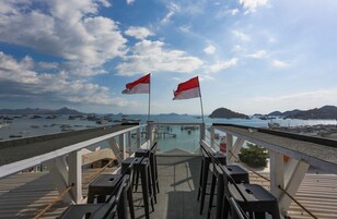 Una terraza con sillas y mesas que da a un puerto con barcos y un cielo despejado.