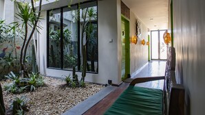 A hallway with a green door, a bed with a green bedspread, and a small garden area with plants and pebbles. - Eco Tree O'tel (Labuan Bajo)