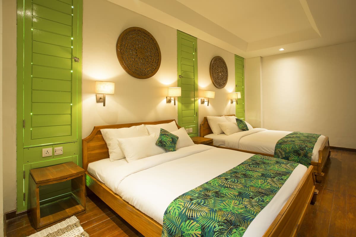 A hotel room with two beds, green shutters, wall-mounted lamps, and a wooden floor.
