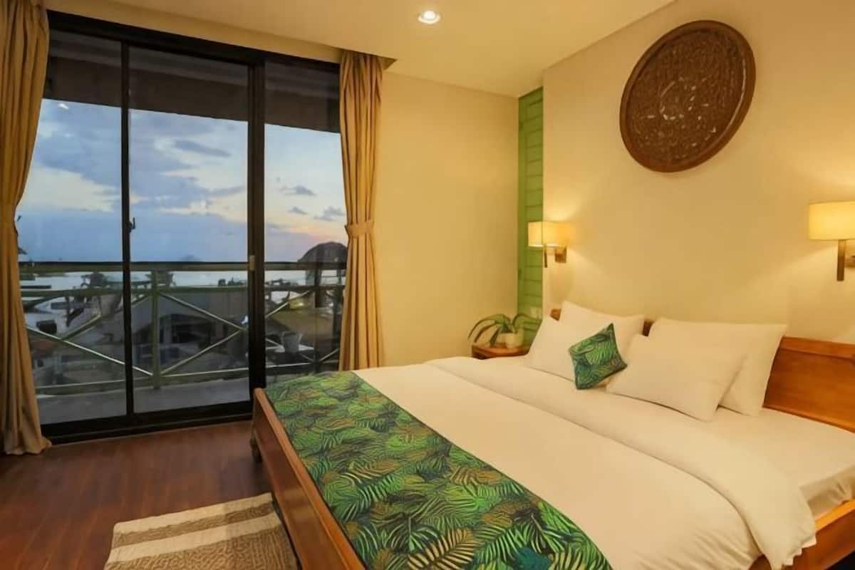 Habitación de hotel con balcón, una cama con cubrecama estampado, una lámpara fijada a la pared y un adorno mural.
