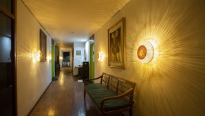 A hallway with a bench, wall-mounted lights, and a painting. - Eco Tree O'tel (Labuan Bajo)