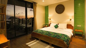 A bedroom with a large bed, a green wall, a round decorative item above the bed, and a view through a glass door. - Eco Tree O'tel (Labuan Bajo)