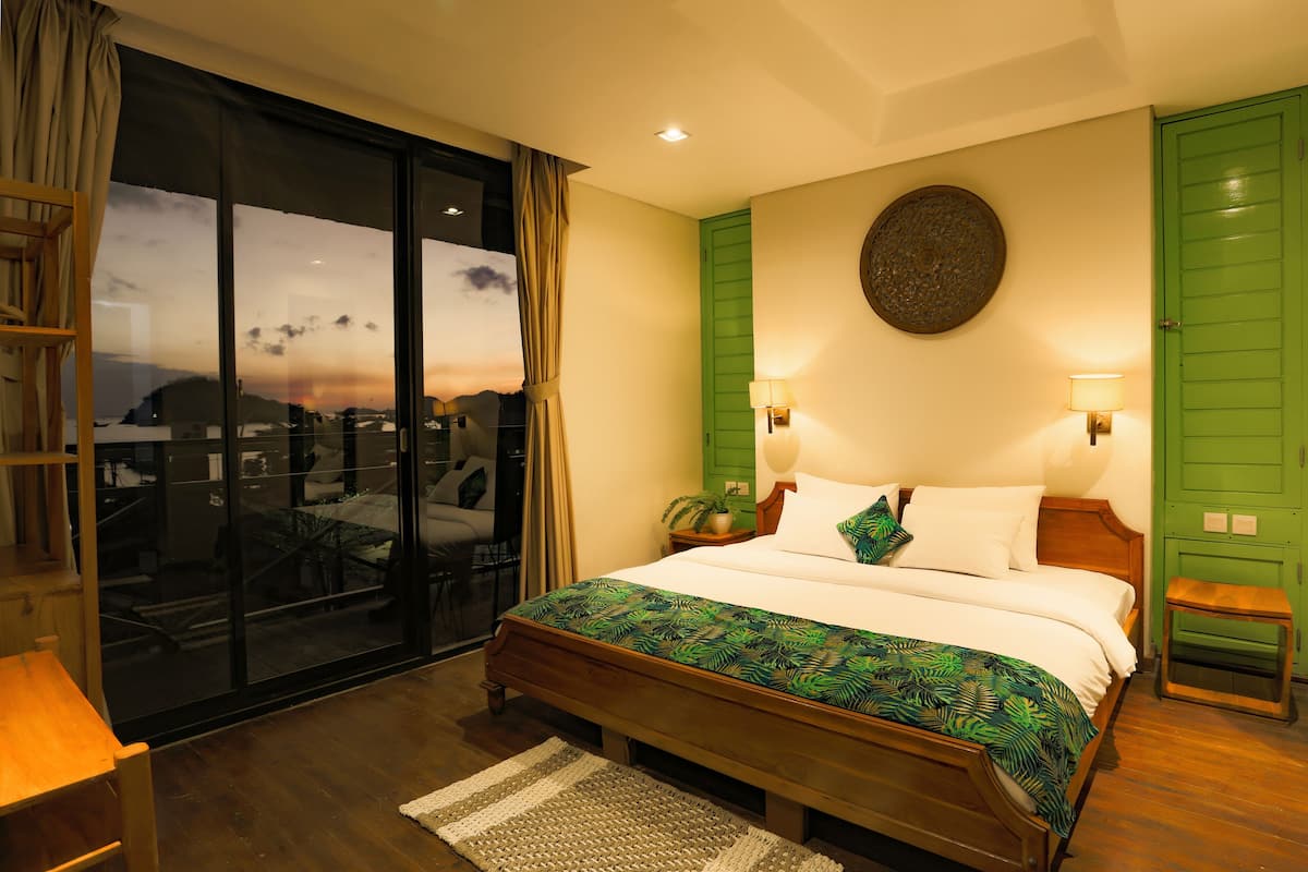 A bedroom with a large bed, a green wall, a round decorative item above the bed, and a view through a glass door.