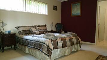 A bedroom with a bed, a nightstand, a lamp, a window with blinds, a painting on the wall, and a door.
