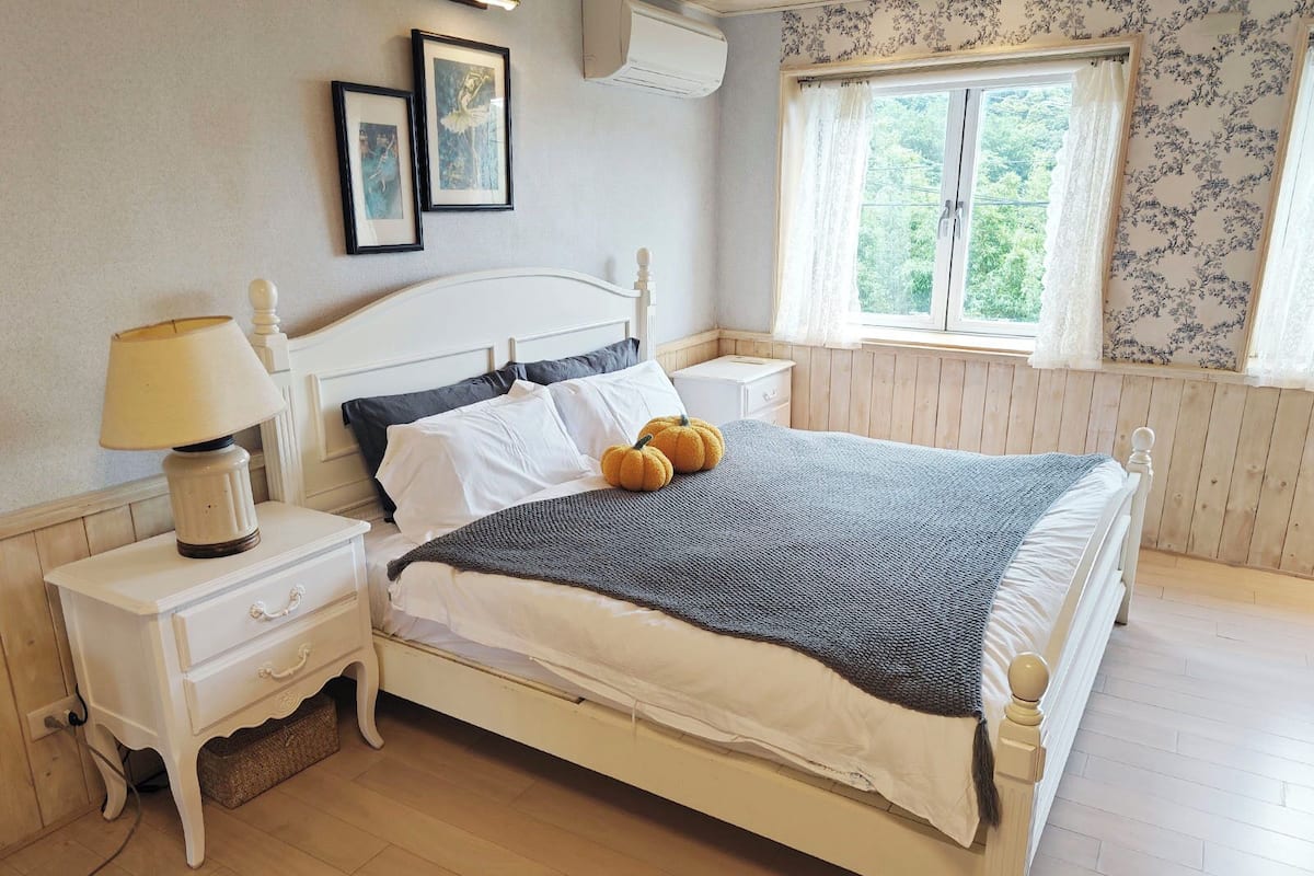 A neatly made bed with a white headboard, a bedside table with a lamp, and a window with curtains.