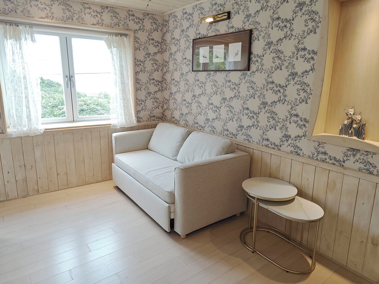 A room with a beige sofa, a small round table, and floral wallpaper.