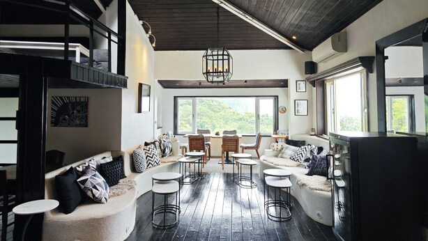 A modern interior with a high ceiling, a cozy seating area with a sofa and chairs, a dining table, and a large window offering a view of the outdoors. - Gold Stone Crescent Moon Light (New Taipei City)