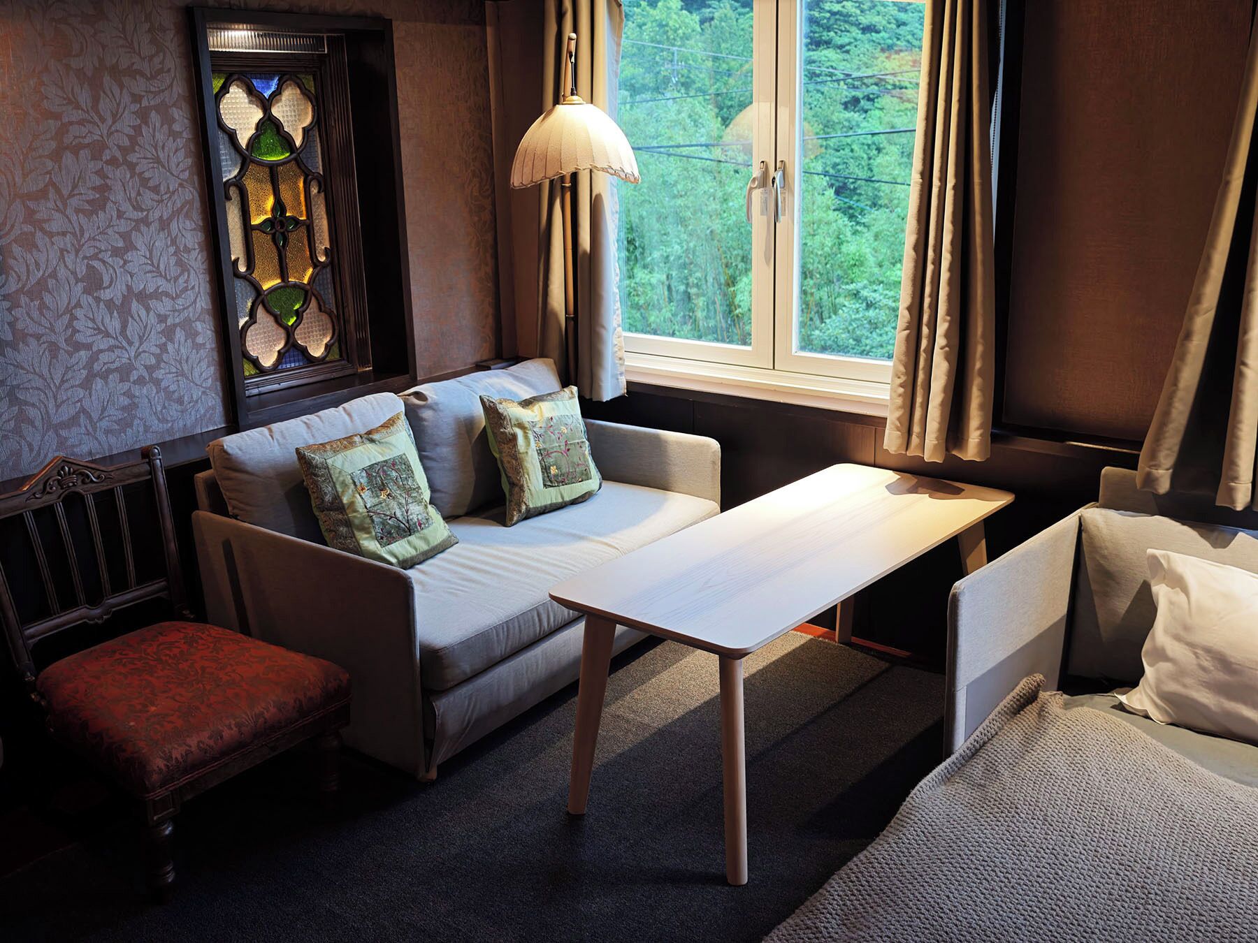 A cozy room with a sofa, a small table, a bench, and a window with curtains.
