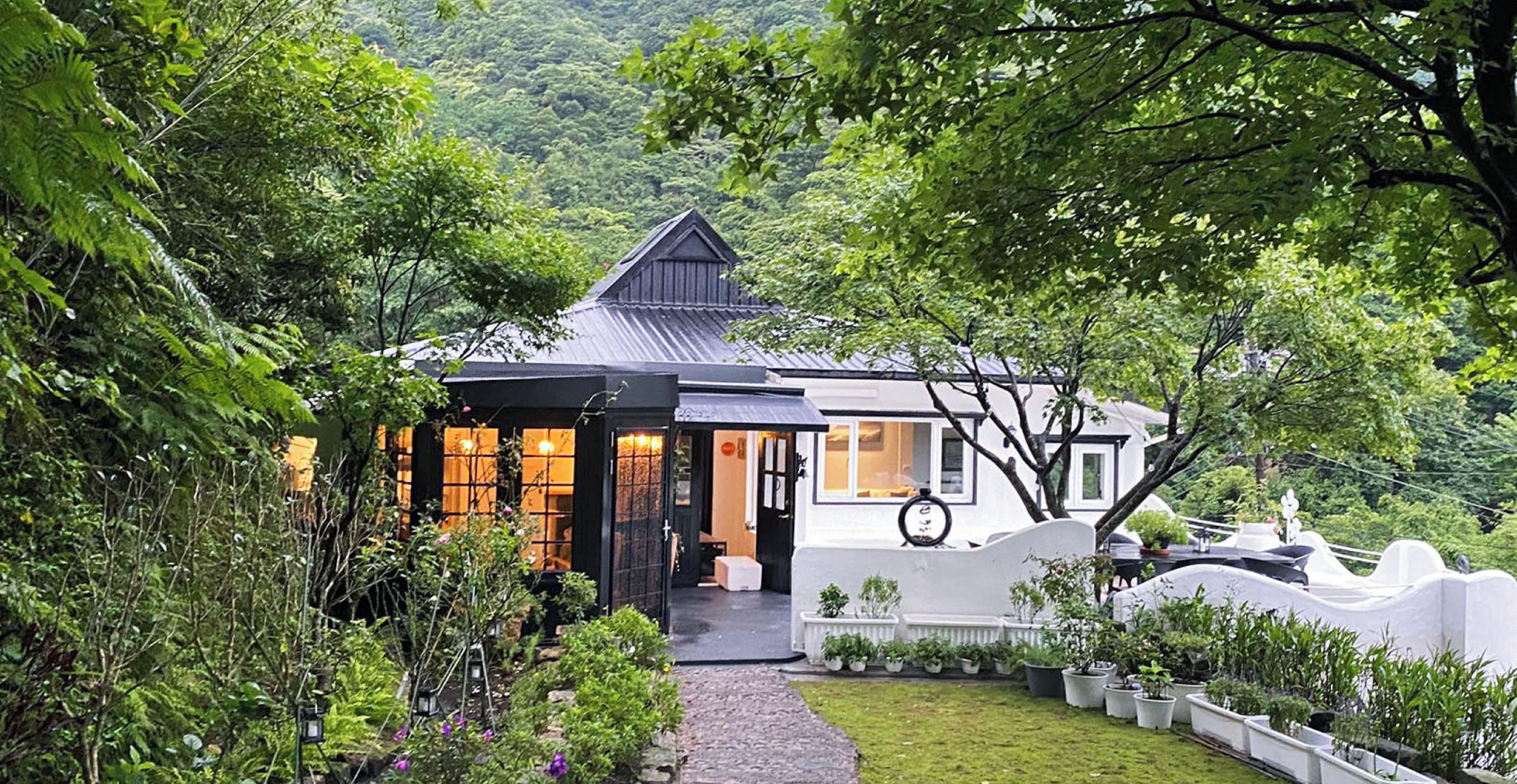 A house with a dark roof, white walls, and a garden with various plants.