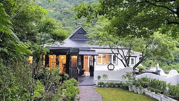 A house with a dark roof, white walls, and a garden with various plants.