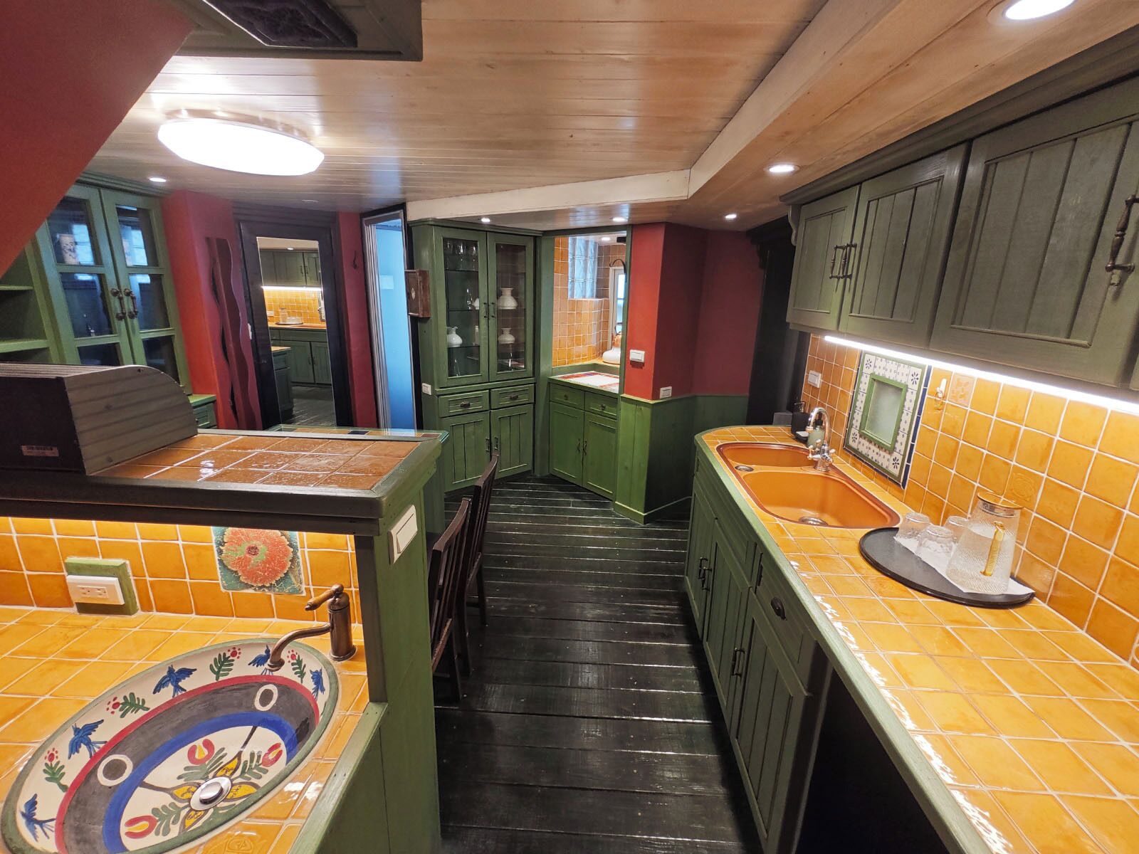 A narrow kitchen with green cabinets, a tiled backsplash, and a wooden floor.