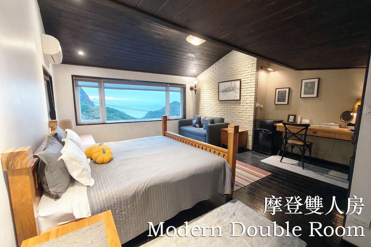 A modern double room with a bed, a desk, and a view of the outdoors.