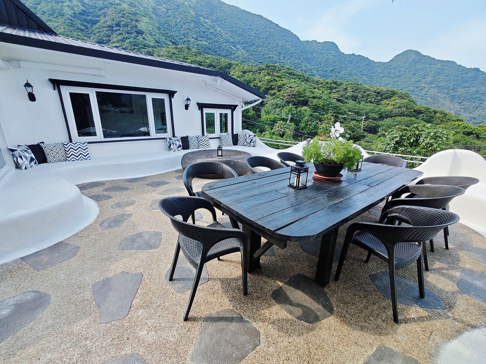 A patio with a table and chairs, surrounded by a white wall and a mountain view.