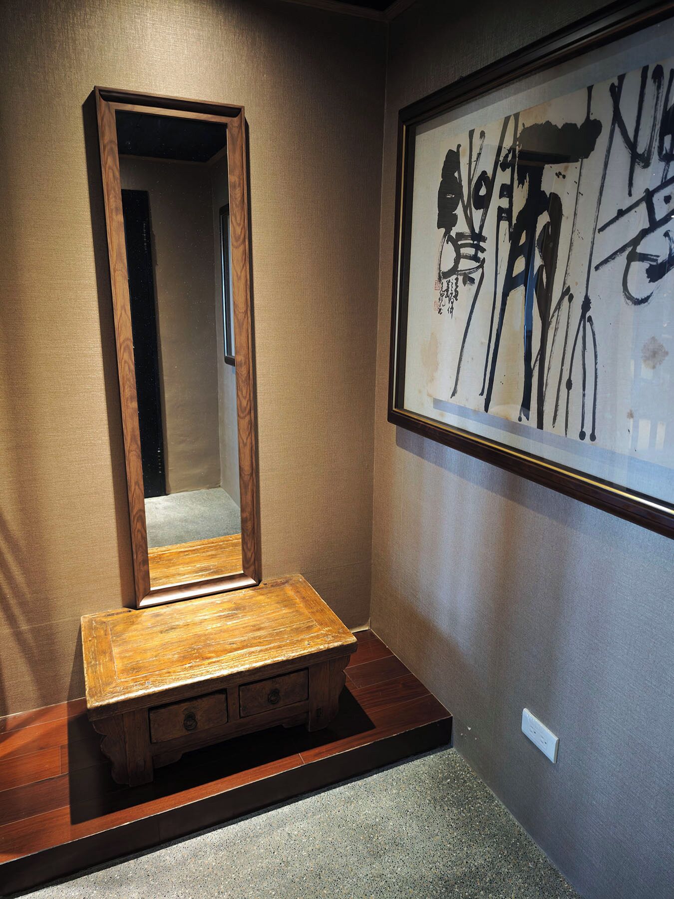 A wooden vanity with a mirror, a small wooden cabinet, and a framed abstract painting on the wall.