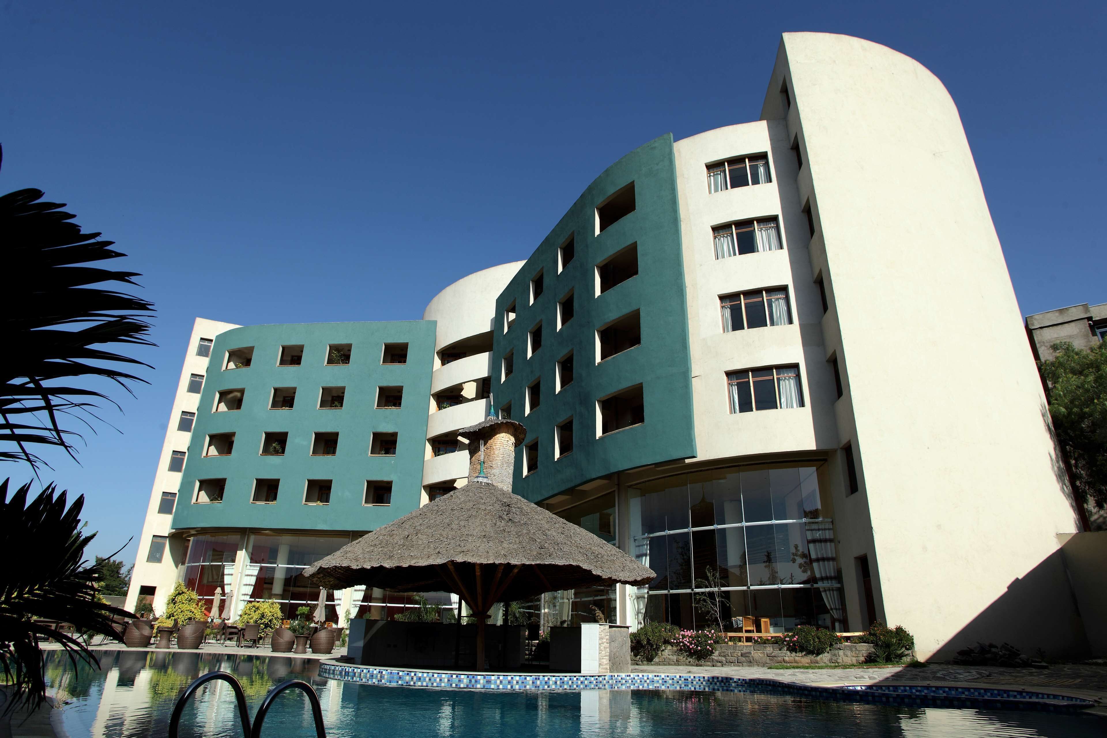 A hotel with a swimming pool, a thatched-roof gazebo, and a modern building with multiple balconies.