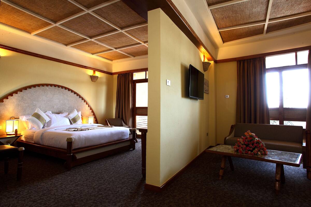 A hotel room with a large bed, a sofa, a coffee table, and a TV mounted on the wall.