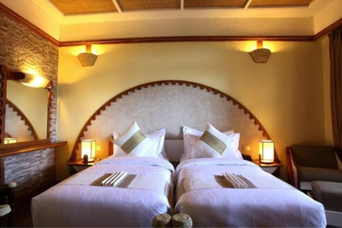 A hotel room with two beds, a large arched headboard, and wall-mounted lamps.