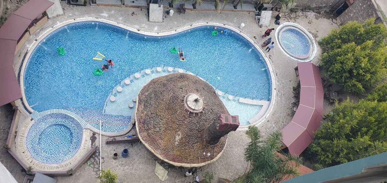 Una amplia piscina exterior con una isla central, rodeada de zonas de descanso y árboles.