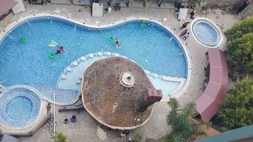 Una amplia piscina exterior con una isla central, rodeada de zonas de descanso y árboles.
