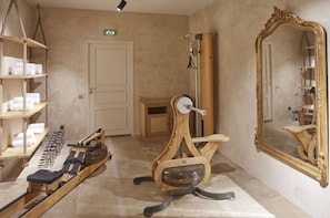 A room with a wooden rowing machine, a large mirror, and shelves with towels.