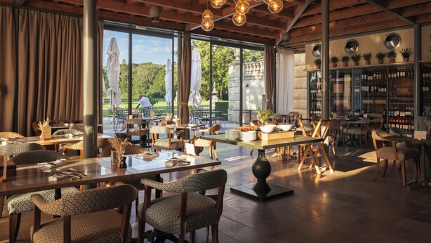 Een ruime restaurant met hoge plafonds, grote ramen en diverse zithoeken.