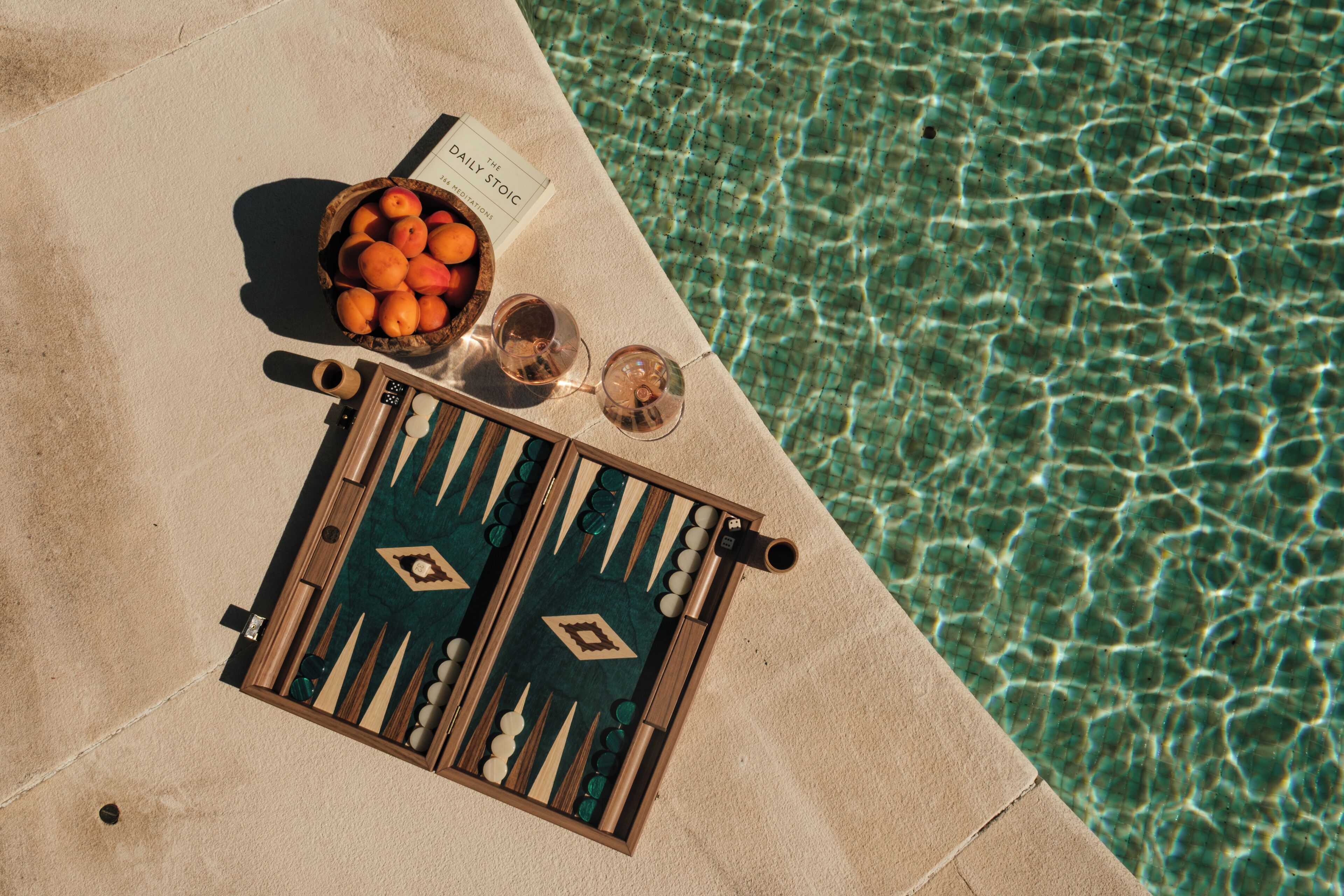 Una mesa junto a la piscina con un juego de mesa, un bol de fruta y un menú.