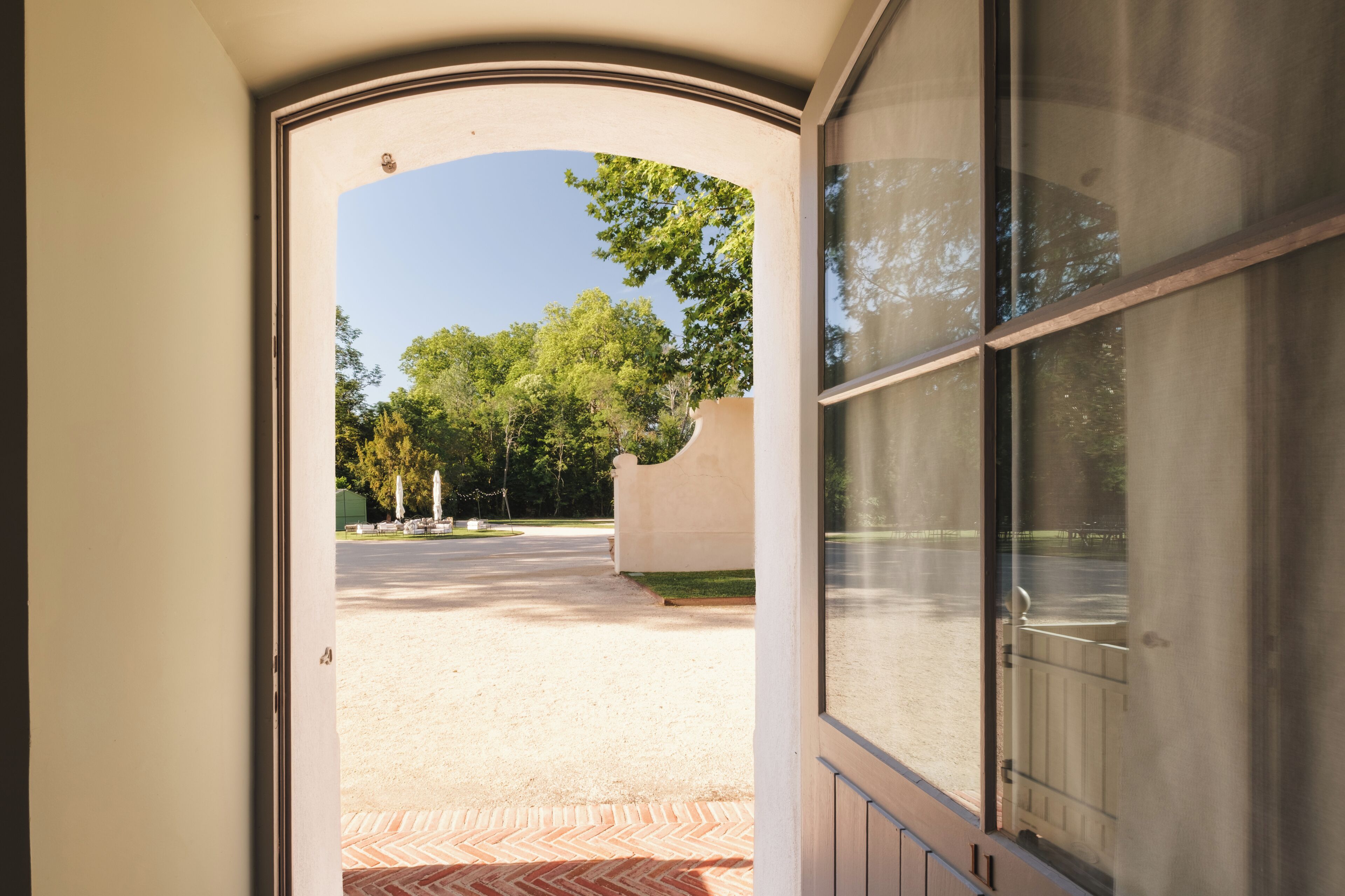 An open door leading to a paved area with trees and a building in the background.