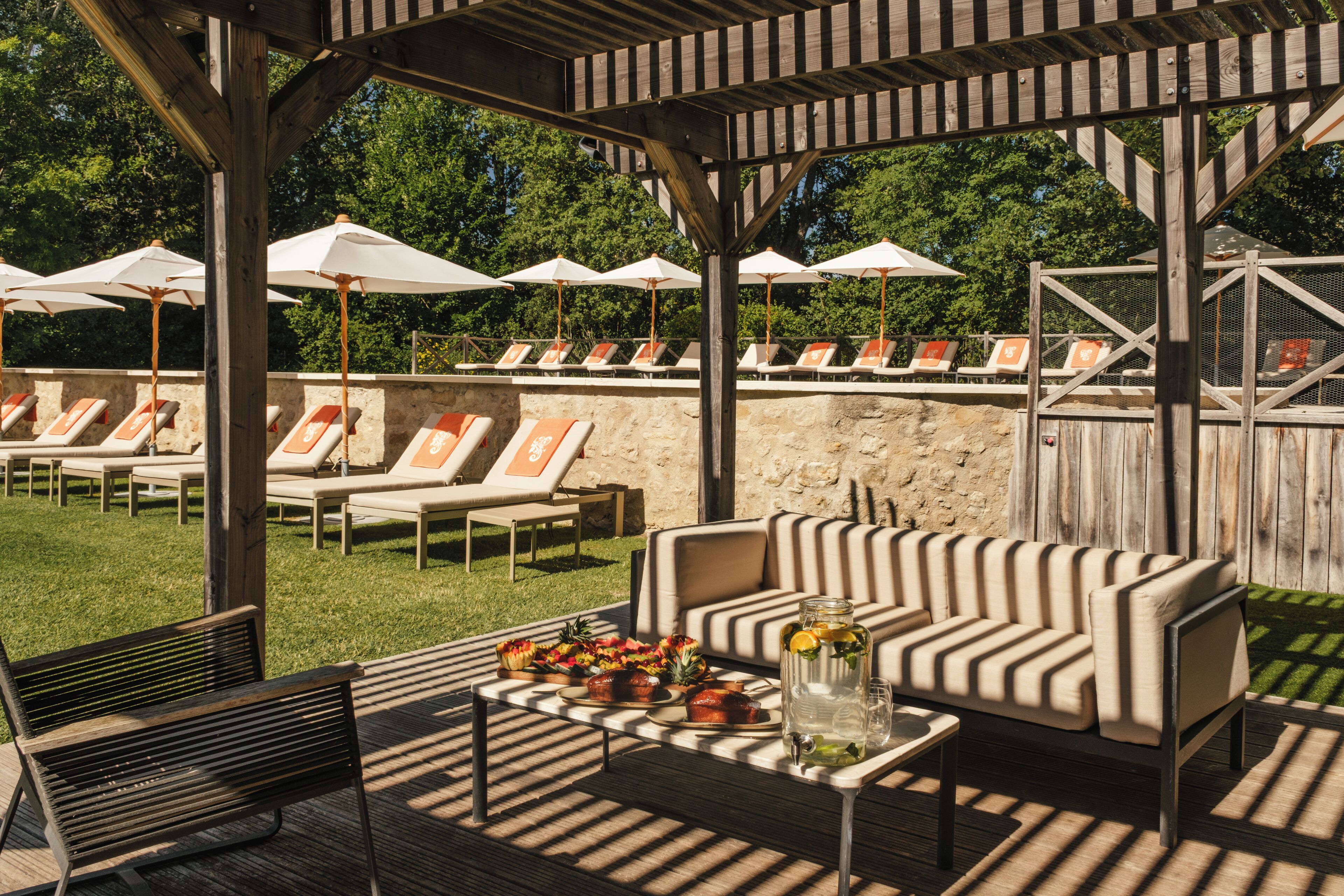 Un espace extérieur abrité, aménagé avec des fauteuils confortables, un canapé et une table où sont servis des plats et des boissons.