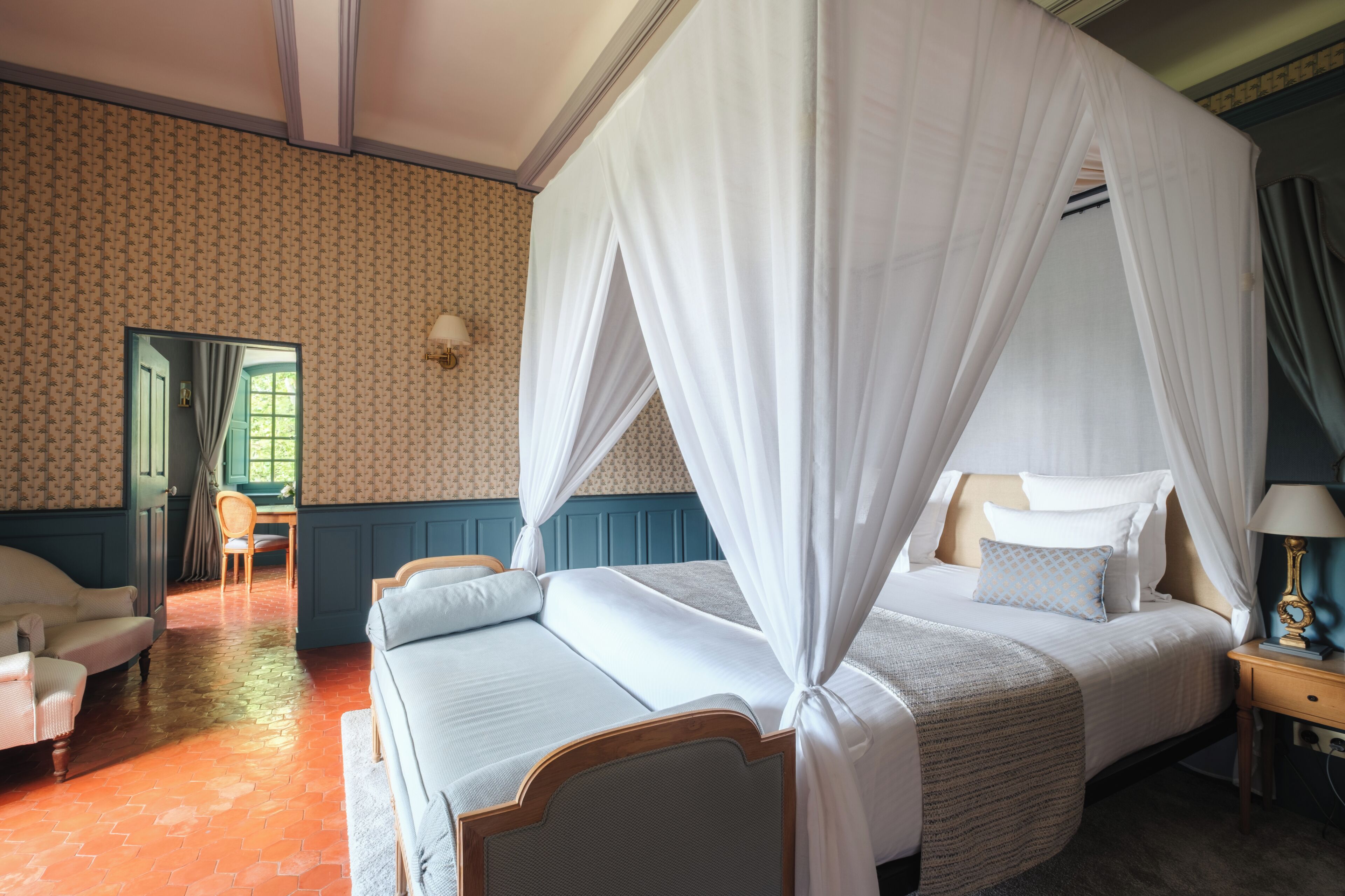 A four-poster bed with white bedding, a wooden headboard, and a nightstand with a lamp.