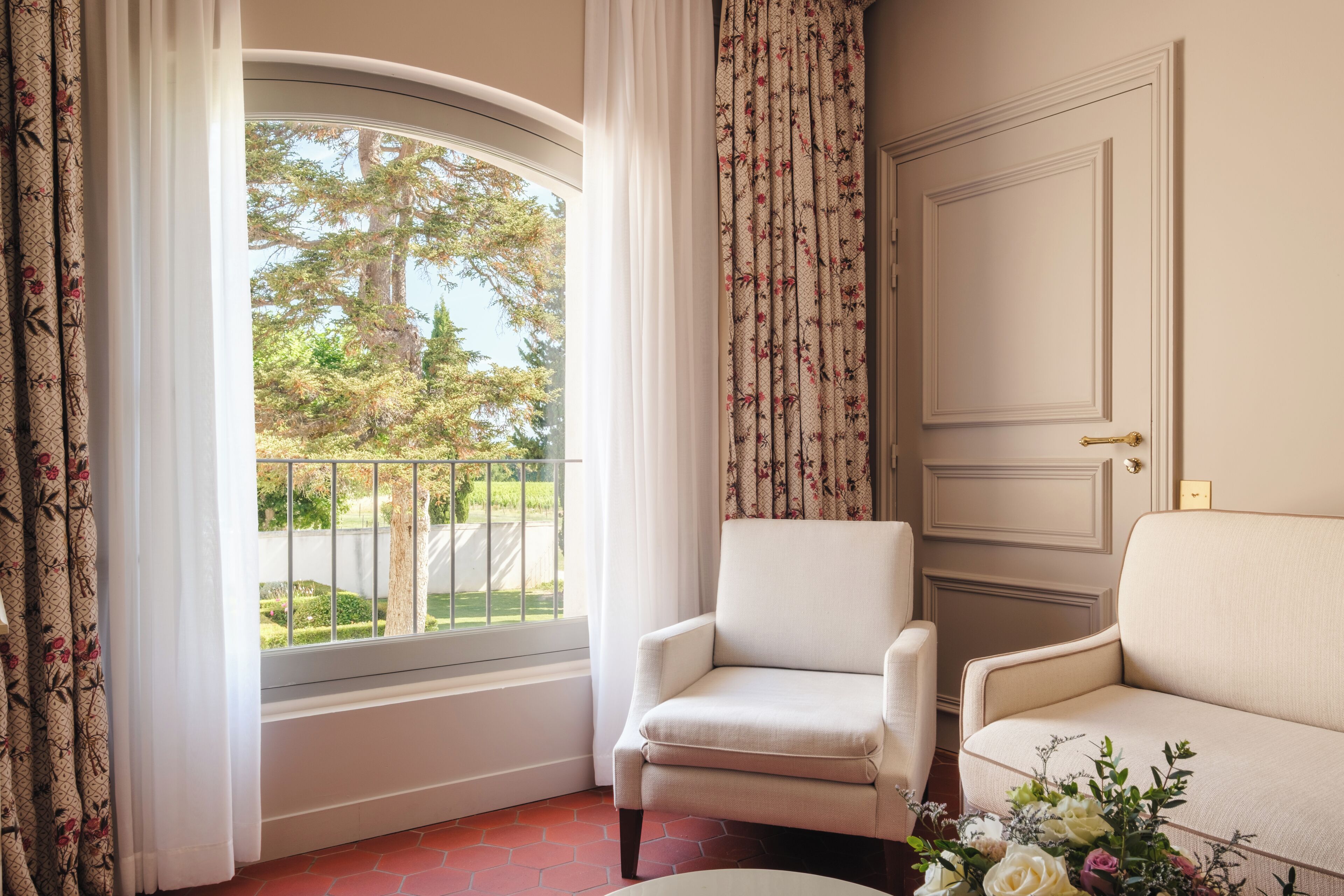A room with a window, two armchairs, a door, and a floral arrangement.
