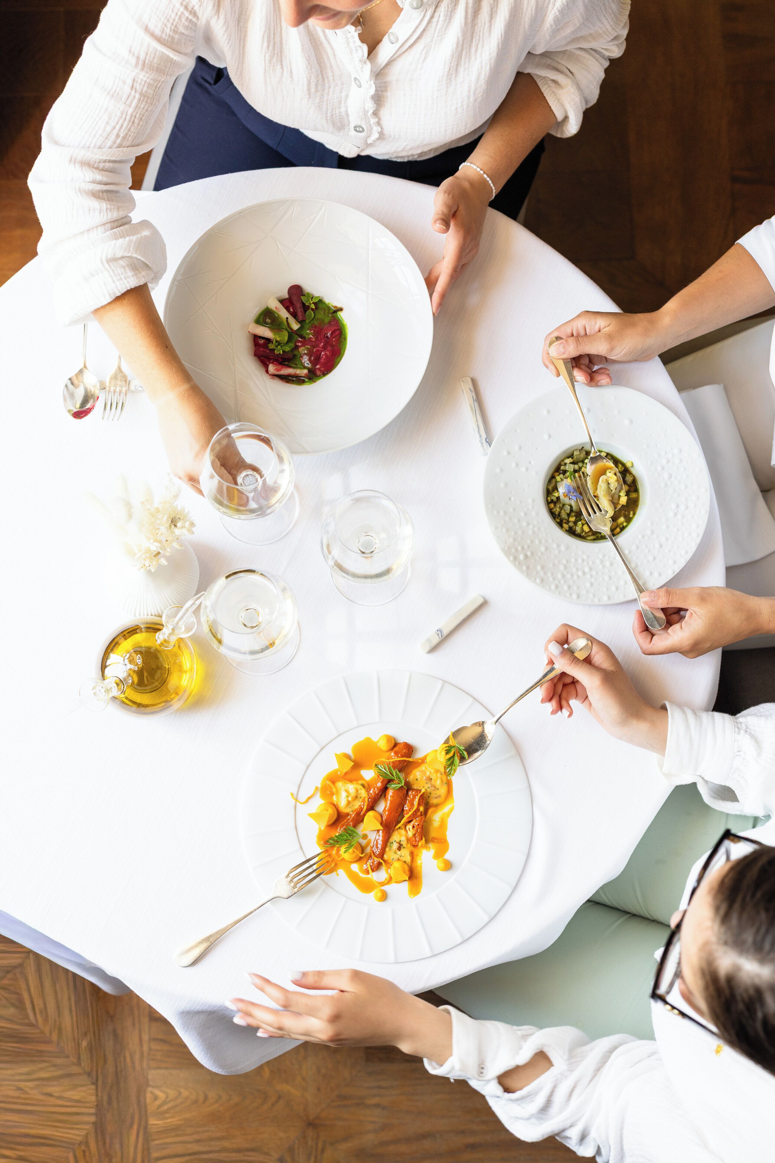 Una mesa de comedor con varios platos de comida, vasos y una botella de aceite de oliva.