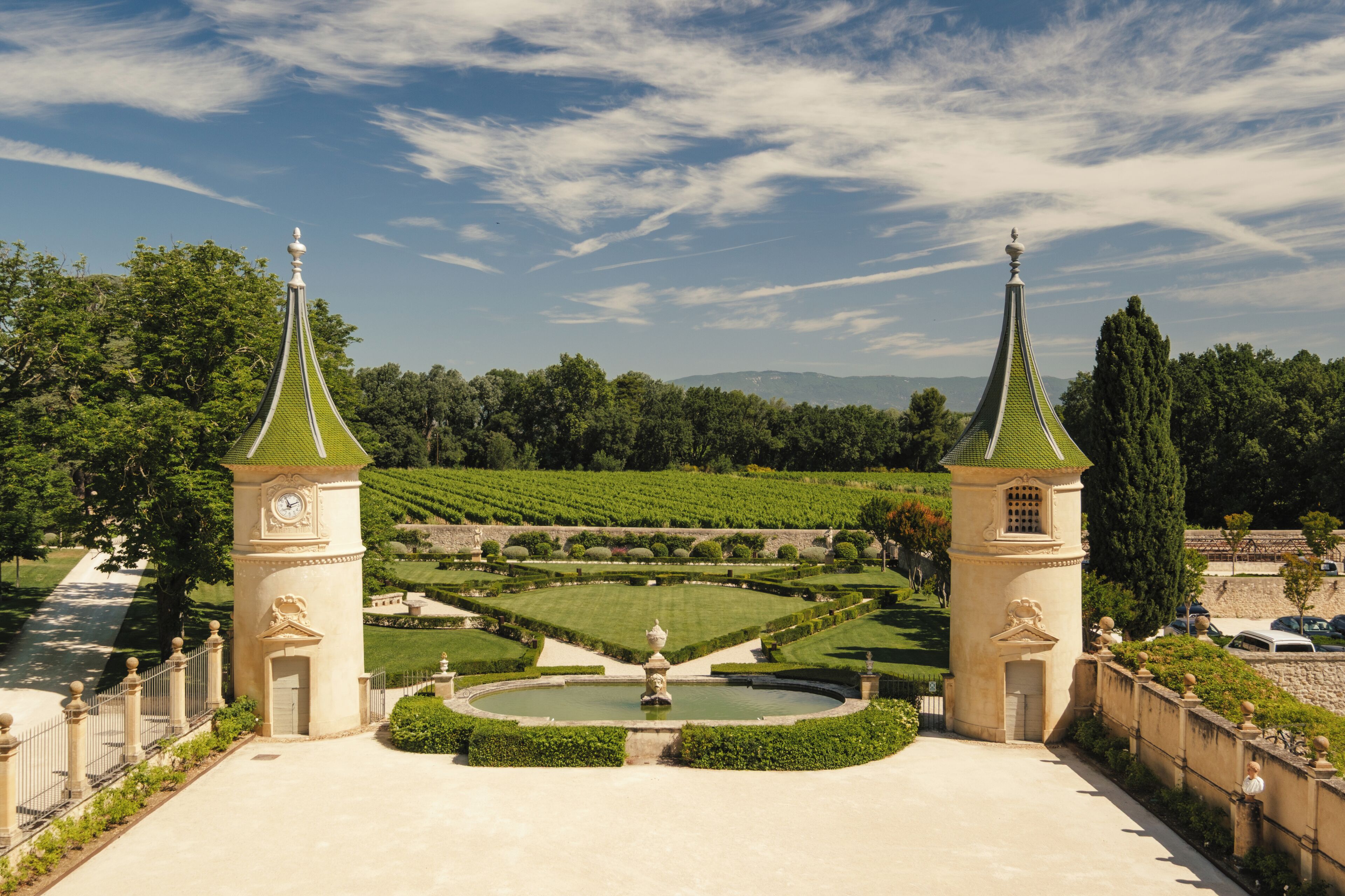 A formal garden with two towers, a central fountain, and a manicured lawn.