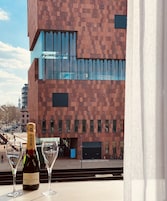Una botella de Moët & Chandon y dos copas sobre una mesa, con vistas a un edificio moderno de fachada de ladrillo y ventanas amplias.
