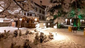 A snow-covered courtyard with a wooden gazebo, snow-laden trees, and a building with illuminated windows in the background. - Safranbolu Asmalı Konak Hotel (Safranbolu)
