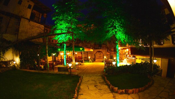 A courtyard with stone pathways, green-lit trees, and a central archway leading to a building. - Safranbolu Asmalı Konak Hotel (Safranbolu)