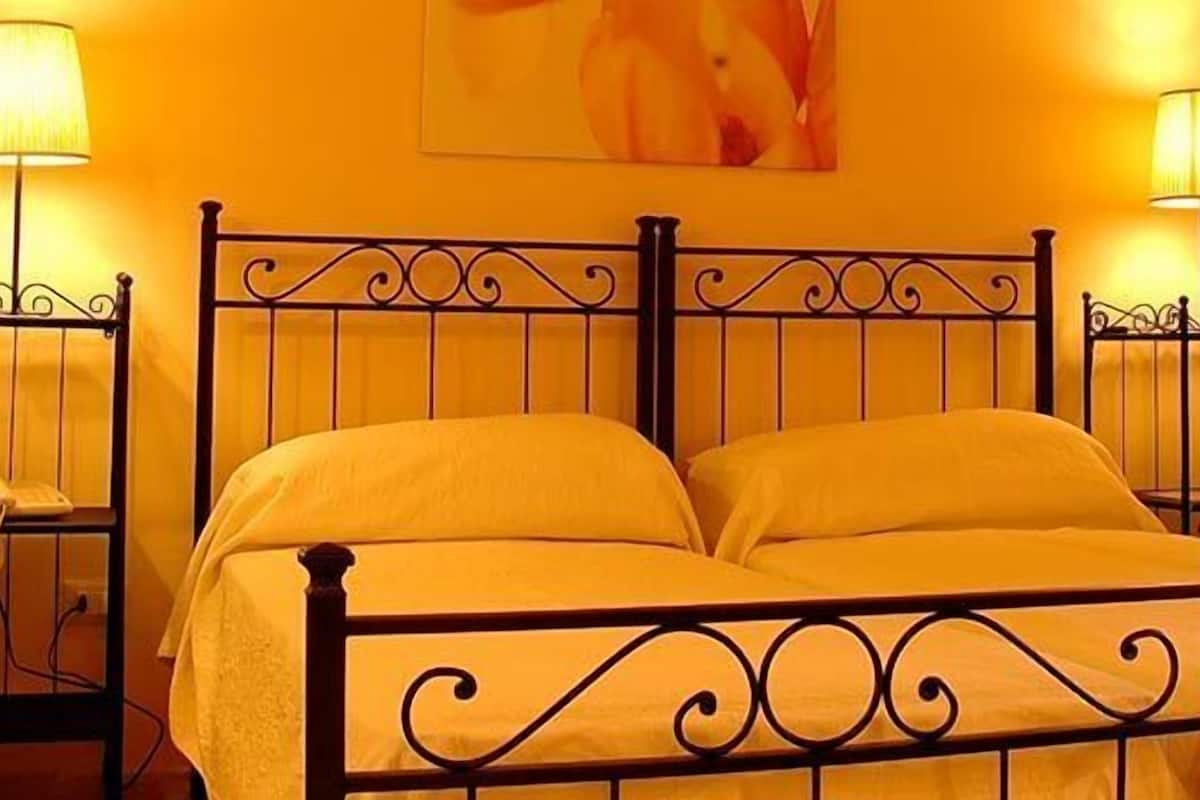 A room with a bed, two bedside lamps, a small table with a telephone, and a wicker chair.