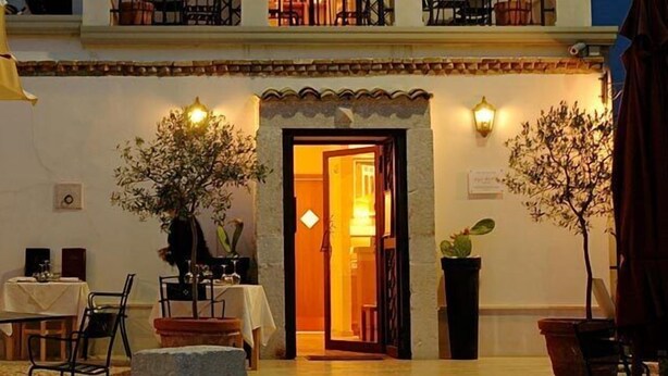 An outdoor dining area with tables and chairs, a yellow umbrella, and a doorway leading to an interior space. - The Olive Inn (Lesina)