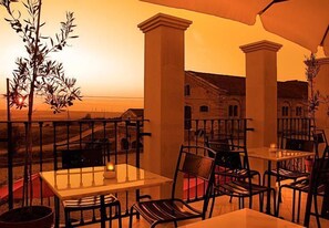 An outdoor dining area with tables and chairs, a view of the countryside, and a sunset in the background. - The Olive Inn (Lesina)