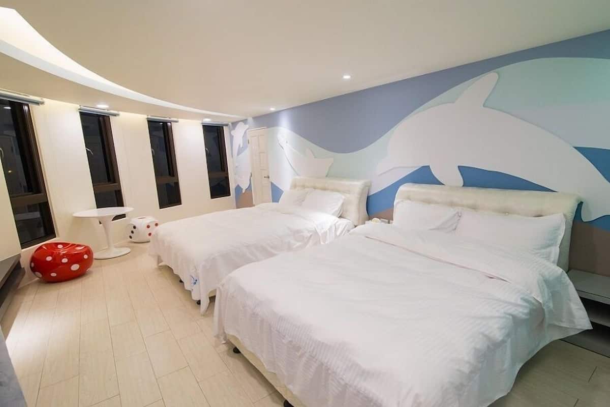 A hotel room with two beds, a large dolphin mural on the wall, a red polka dot chair, and a white table.