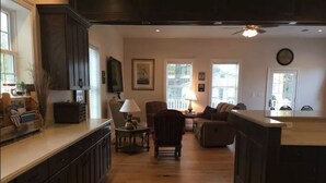 A spacious kitchen with wooden cabinets, a dining area with a table and chairs, and a living room with a sofa and a lamp. - Crystal Run Suites of Springboro (Springboro)