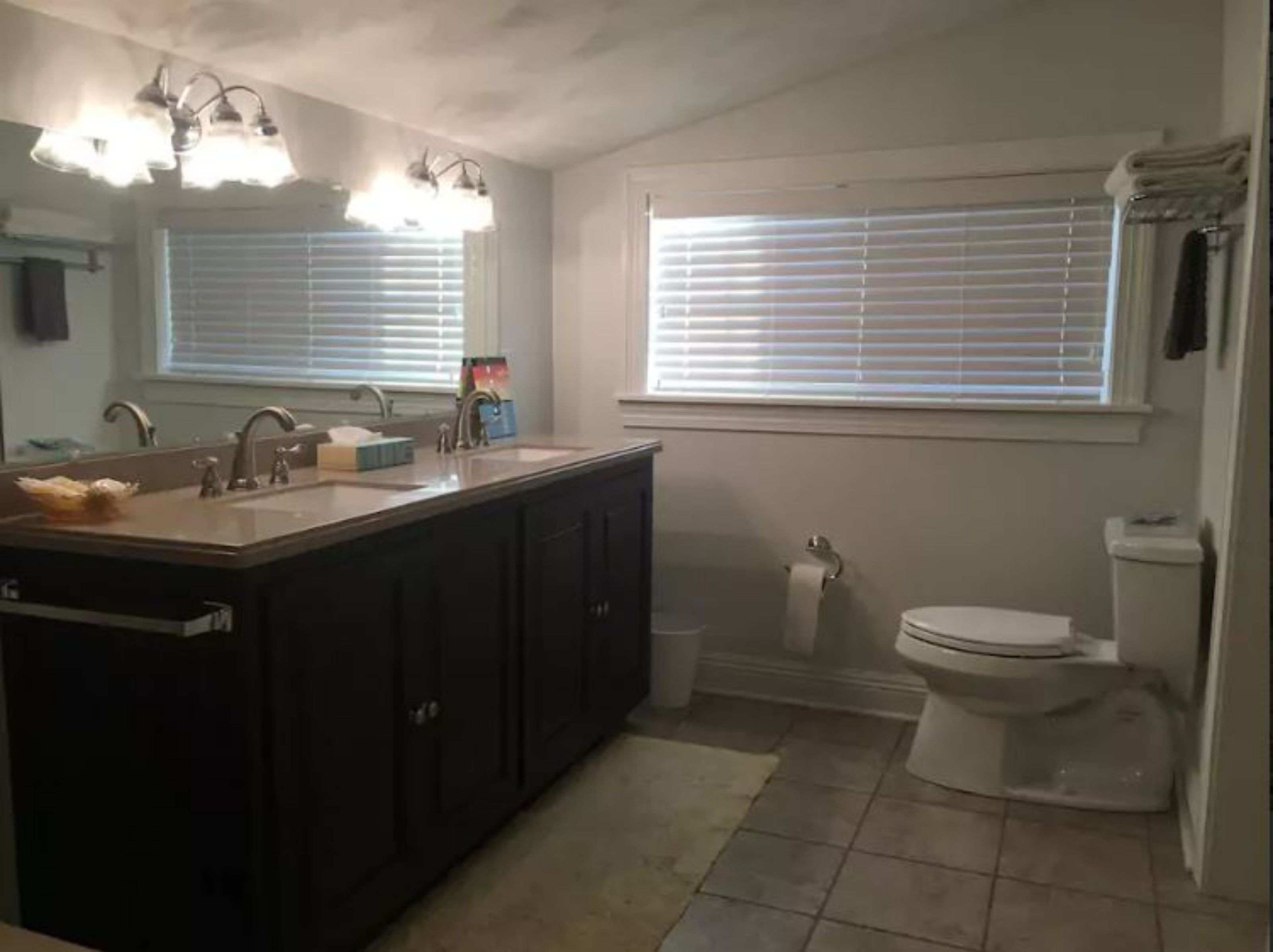 Une salle de bain avec un lavabo, un miroir, des toilettes et une fenêtre.