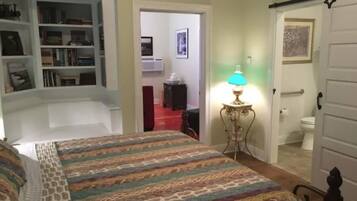 A bedroom with a bed, a bookshelf, a lamp, and a door leading to a bathroom.