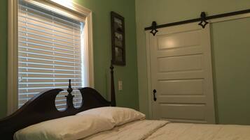 A bedroom with a bed, a window with blinds, a door with a black handle, and a wall-mounted picture.