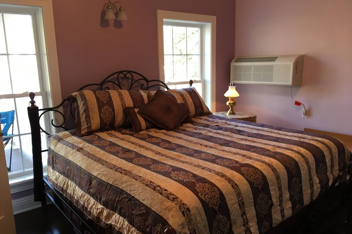 A bedroom with a bed, a nightstand, a lamp, and an air conditioning unit.