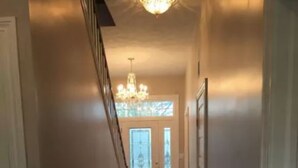 A hallway with wooden flooring, white walls, and a chandelier. - Crystal Run Suites of Springboro (Springboro)